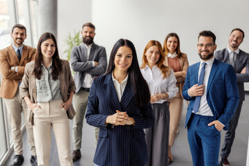 Female leader standing at corporate firm with her team of experts and smiling at the camera.