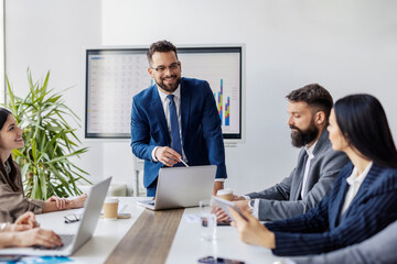 Young executive is standing at boardroom with his team of experts and analyzing data and financial reports.