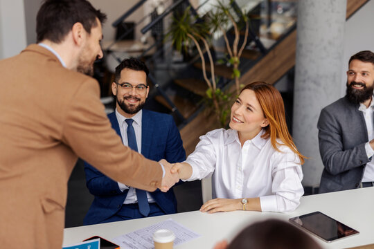 An executive standing at boardroom and congratulating businesswoman on a success in front of team of experts.