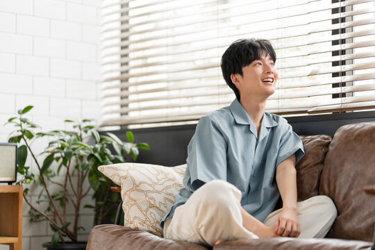 ソファーに座り部屋の中から窓の外を眺めている若い日本人男性。
