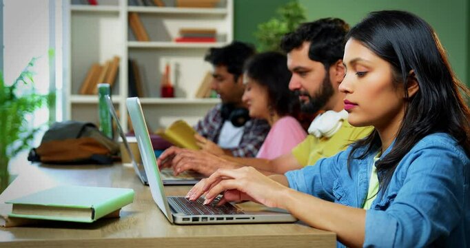Indian college students using laptop to complete assignment with books, notes, preparing for exams studying in a focused, collaborative environment inside a university campus library in exam season