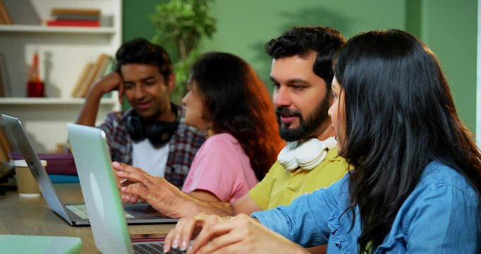 Indian college students using laptop to complete assignment with books, notes, preparing for exams studying in a focused, collaborative environment inside a university campus library in exam season