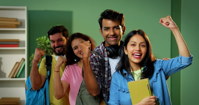 College students celebrating success with smiles raised hands, Indian university group standing indoors showing positive emotions, joy, team spirit after achieving academic or milestone together