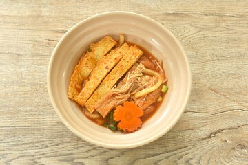 udon noodles topping slice fish tofu and needle mushroom with carot in kimchi soup on bowl