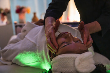 Beautician massaging face of woman during a treatment in a beauty center with green light therapy