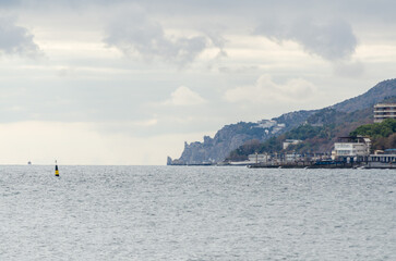 Expansive seascape featuring calm water and distant shoreline. Overcast sky creates muted...