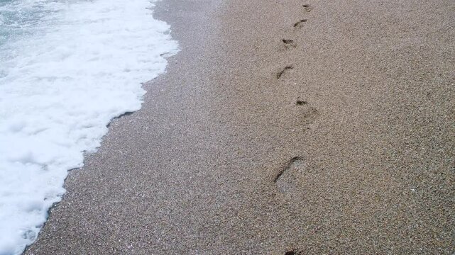 A man walking along the sea has left footprints in the sand, which will be washed away by the surf.