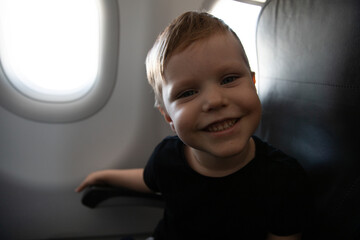 Little Boy On Plane Sitting At Window Satisfied In Black T-Shirt