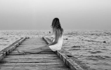 the woman in meditation sitting on the pier in front of the sea at sunset
