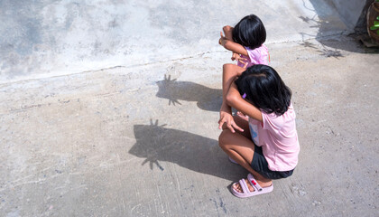 Two Asian female children are gesturing to making shadow look like cat shape on concrete floor in...