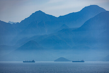 Telephoto shot of Taurus Mountains in blue haze with two cargo ships anchored offshore. Industrial meets nature in Antalya, Turkey. © Vlad Rakin
