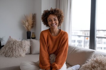 A happy African American young woman is depicted sitting on a sofa at home, symbolizing people, race, ethnicity, and portrait concepts
