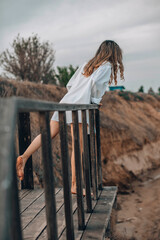 unrecognizable woman in white shirt standing barefoot on wooden platform with one foot raised, natural cliff landscape, back view, solitude, personal reflection, nature retreat