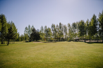 Sunny view of a golf course fairway with a sand bunker and trees lining the background, under a...