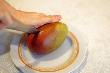 A woman cuts a ripe mango with a knife on a plate