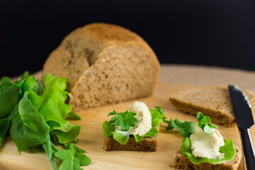 Slice of rye bread with cheese spread and greens on the table