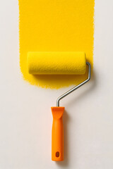 Obraz premium Bright yellow paint roller on white wall with orange handle