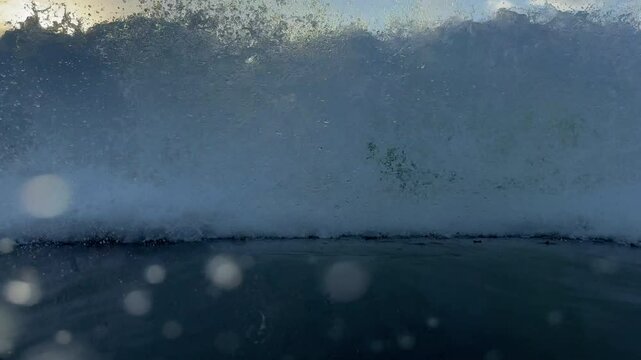 Dreamy green backlit ocean wave curls and breaks below a warm morning sun, exploding into a wall of white water. Captured from in fromt and below the ocean in slow motion.
