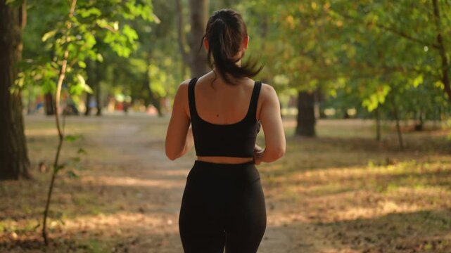 A woman jogs through a tranquil, peaceful park, fully embracing both nature as well as her fitness journey - Powered by Adobe