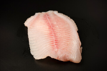 Fresh tilapia fillet on black background, top view.