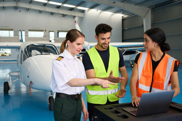 Pilot and mechanics discussing maintenance using laptop in hangar