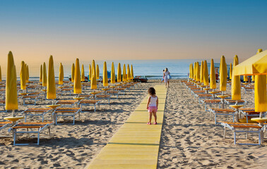 a little girl walks towards her mother on a beach walkway
