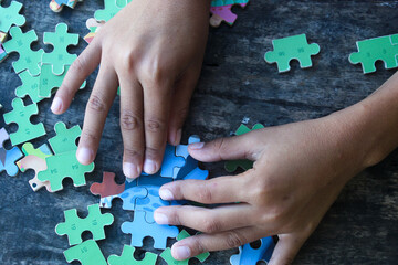 hands playing jigsaw puzzle on wooden table