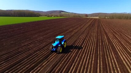 Aerial view of a blue tractor cultivating a plowed field - Powered by Adobe
