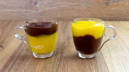 Two Glass Mugs with Layered Chocolate and Pastry Cream Dessert on Wooden Table