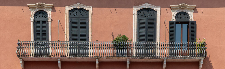 Historic Italian Building Facade with Ornate Balcony and Traditional Green Shutters