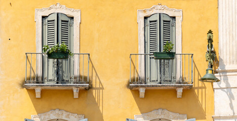 Traditional Italian Building Facade with Ornate Balconies and Green Shutters Against Warm Yellow Wall