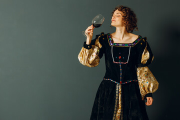 Young adult woman dressed in a medieval dress holding a glass of wine and drinking a red wine
