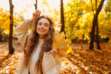 Smiling young woman holds yellow leaf in her hand in the park at sunset