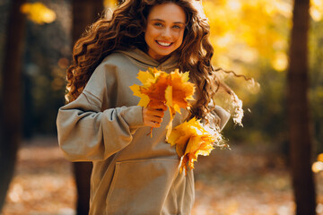 Smiling young woman enjoys the autumn weather in the forest with the yellow leaves at sunset
