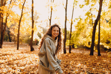 Smiling young woman enjoys the autumn weather in the forest with the yellow leaves at sunset