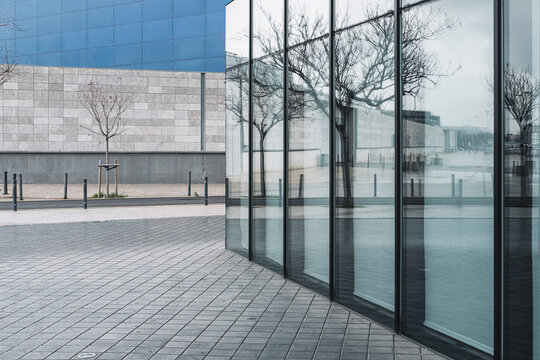 Glass facade reflecting urban trees and empty plaza, modern architectural detail in London cityscape, ideal for abstract and business design applications.
