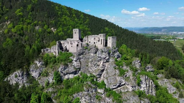 Drone footage reveals the majestic ruins of Strečno Castle perched dramatically on a limestone cliff above the V&aacute;h River, surrounded by the lush, mountainous forests of northern Slovakia