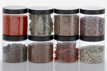 Collection of various spices in round containers with black lids on white background.