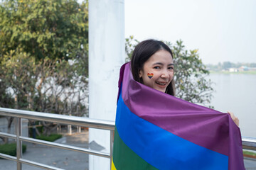A joyful young woman proudly displays a rainbow flag, symbolizing love and diversity, with a river backdrop. Celebrating inclusivity and unity.