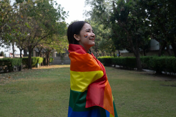 A joyful individual wrapped in a rainbow flag, celebrating pride and embracing diversity, amidst a serene outdoor setting with lush greenery.