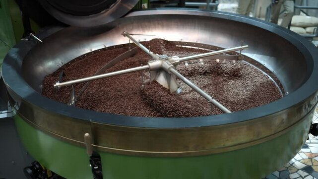 Slow rotation stirs freshly roasted coffee beans inside a shiny industrial cooling tray creating a calming mechanical rhythm in a premium roastery where precision meets craftsmanship