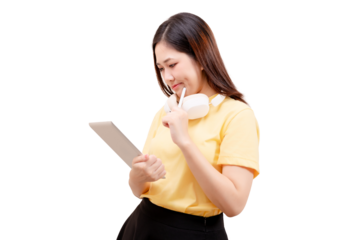 Asian young beautiful woman in a yellow shirt holds a tablet and looks at it thoughtfully with headphones around her neck.