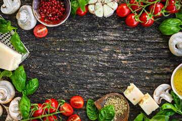 Frame of different ingredients for cooking Italian food. Cherry tomatoes mushrooms parmesan cheese garlic olive oil basil and spices on rustic wooden background with copy space top view