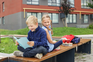 Smiling school kids reading books outdoors.