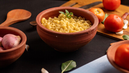 A closeup shot of raw macaroni pasta scattered inside dish,with ingredients placed around it on a  black background. The sharp details enhance its appeal for editorial and marketing use. 