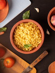 An overhead shot of raw macaroni pasta scattered inside dish,with ingredients and wooden spoon on a chopping board. The sharp details enhance its appeal for editorial and marketing use. 