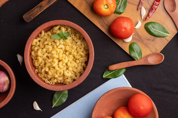 An overhead shot of raw macaroni pasta on the left side of frame,with ingredients placed around it on a  black background. The sharp details enhance its appeal for editorial and marketing use. 