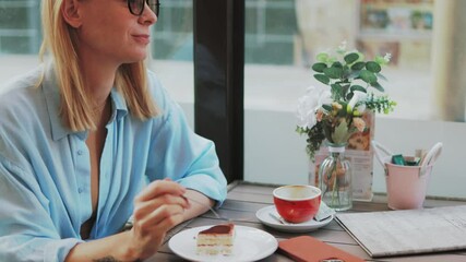 Young businesswoman wearing glasses enjoys a slice of cake and a cup of coffee at an outdoor cafe table, savoring each bite and sip in a relaxing atmosphere