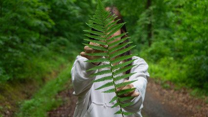 A young woman in a light beige hoodie holding a fern branch in the forest