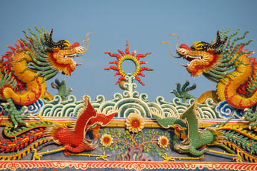 Fototapeta premium Chinese style decoration in buddhist temple. Dragon statues on the roof and st the entrance, sacred place of chinese religion. Dragon face statue in the chinese temple. Red asian dragon in China